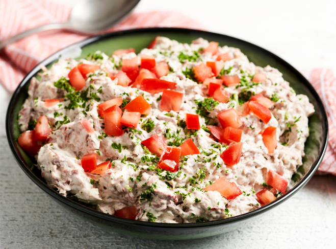 Une salade de thon et de tomates recouverte d'herbes aromatique dans une assiette noire