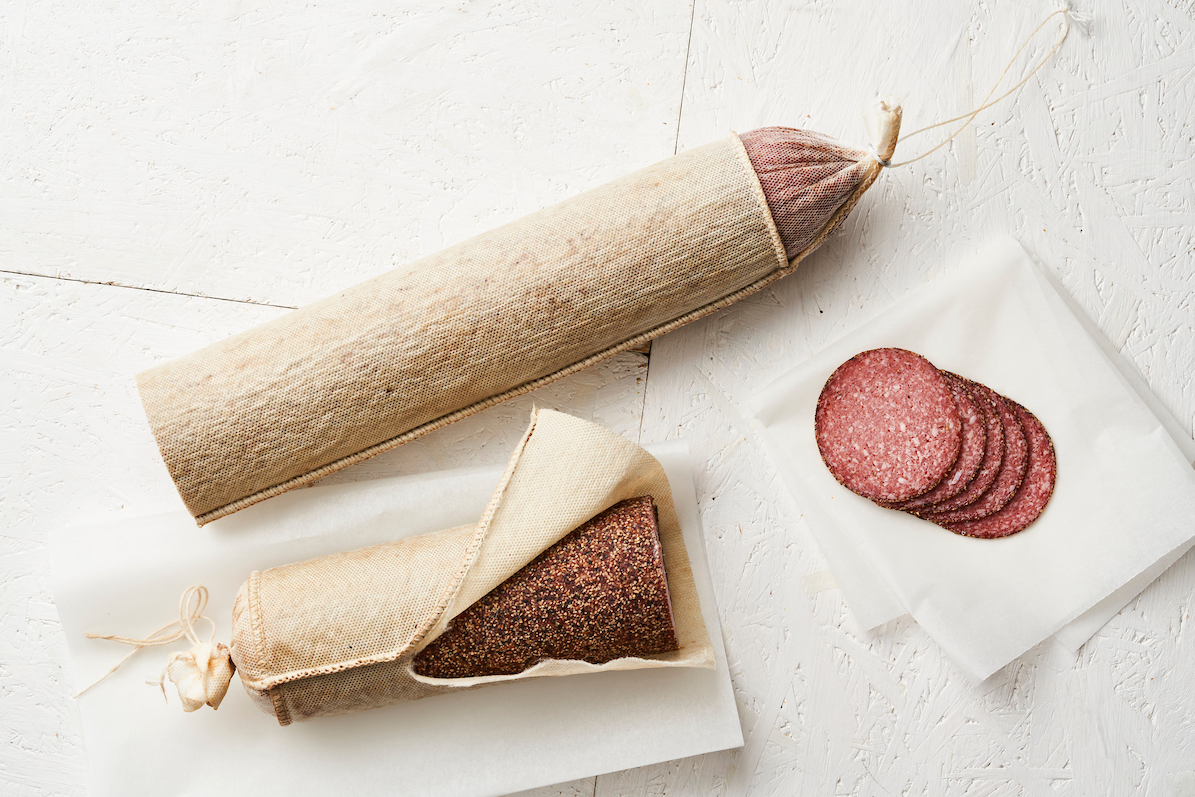 Deux saucissons aux poivre emballés dans du tissu et quelques tranches coupées sur une feuille en papier